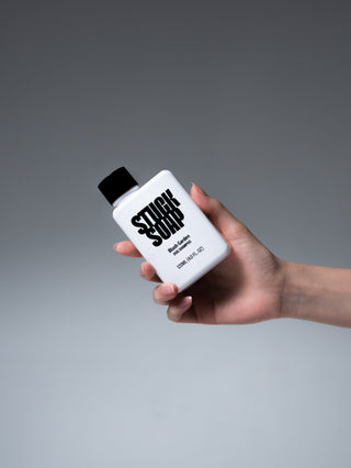 Hand holding a white Blush Garden 120 ml dog shampoo bottle against a grey background
