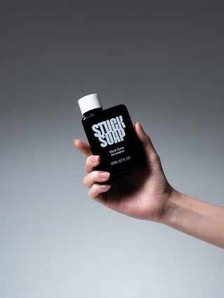 Hand holding a black Silent Grove 120 ml dog shampoo bottle against a grey background
