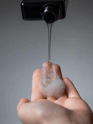 Shampoo pouring from a black Silent Grove bottle into a cupped hand already holding foam
