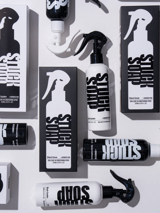 Leave-in spray bottles and their cartons in both scents arranged on a white surface, seen from above