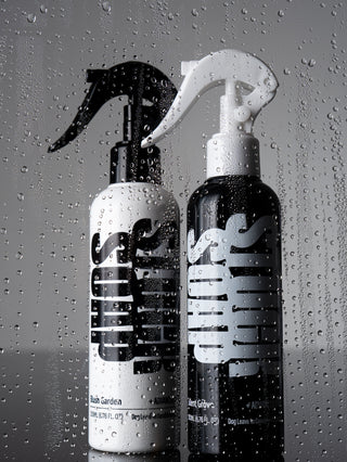 White Blush Garden and black Silent Grove leave-in spray bottles behind a pane covered in water droplets
